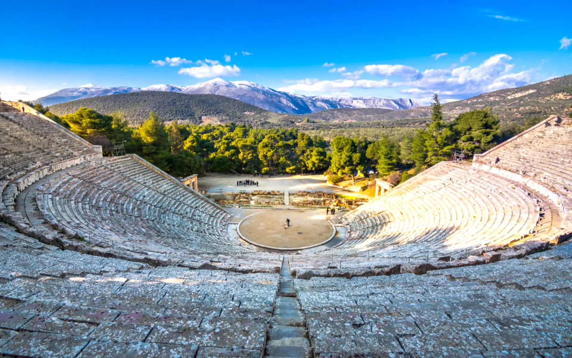 The Great Theatre of Epidaurus surrounded by lush green pine forests in Greece.